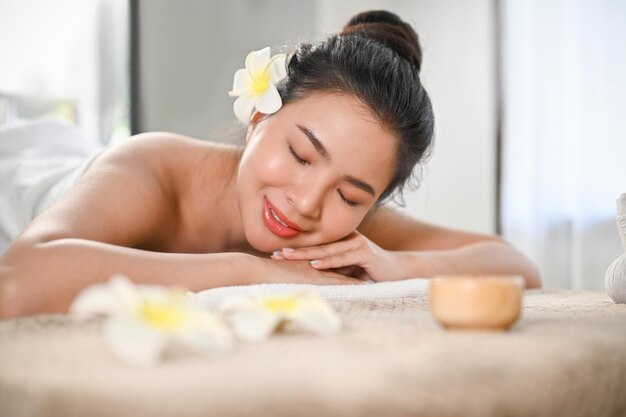 Linda e calma mulher asiática deitada na mesa de massagem com os olhos fechados no salão de spa de beleza