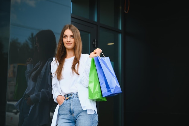 Linda e elegante mulher feliz em pé com sacolas de compras perto de um shopping center na Black Friday