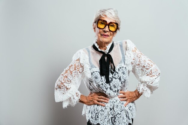 Linda e elegante velha influenciadora. Avó legal posando no estúdio, vestindo roupas da moda. Feliz senhora sênior comemorando e fazendo festa. Conceito sobre antiguidade e estilo de vida