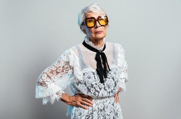 Linda e elegante velha influenciadora. Avó legal posando no estúdio, vestindo roupas da moda. Feliz senhora sênior comemorando e fazendo festa. Conceito sobre antiguidade e estilo de vida