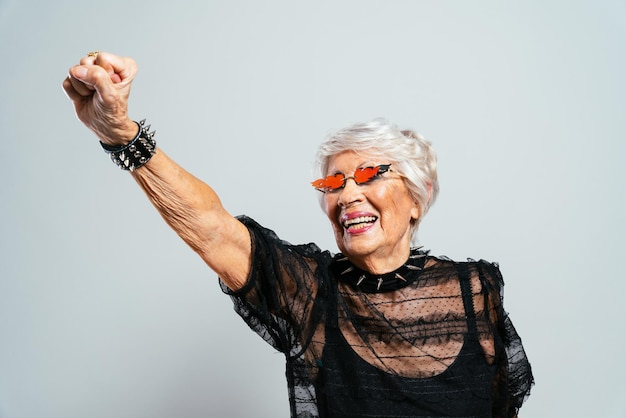 Linda e elegante velha influenciadora. avó legal posando no estúdio, vestindo roupas da moda. feliz senhora sênior comemorando e fazendo festa. conceito sobre antiguidade e estilo de vida