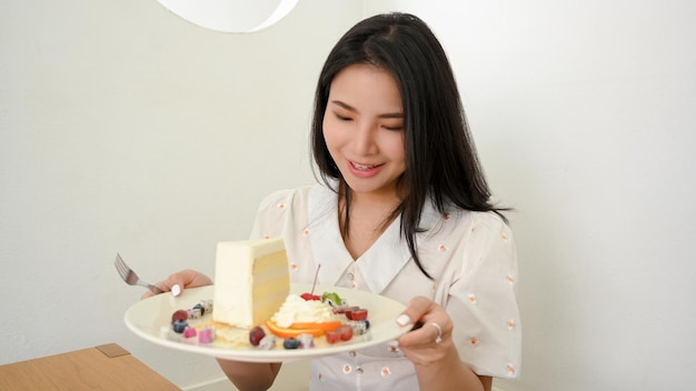 Linda e encantadora mulher asiática milenar segurando um prato de gostoso um pedaço de bolo no café