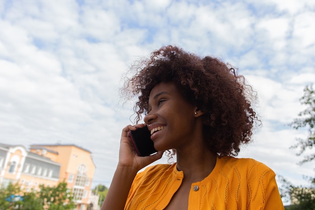 Foto linda e feliz afro-americana na rua com seu telefone