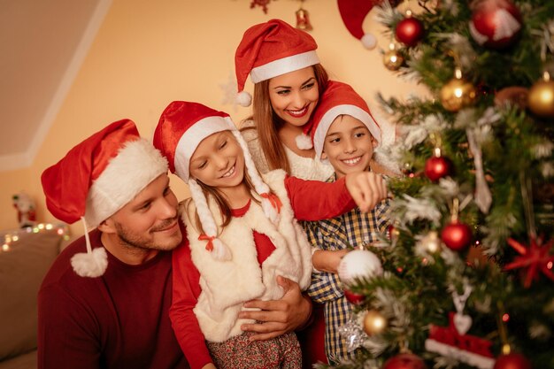 Linda e feliz irmã e irmão decorando a árvore de Natal com seus pais em casa.