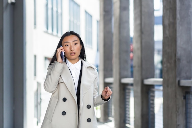 Linda e feliz mulher asiática falando ao telefone, estudante chinês caminha no intervalo