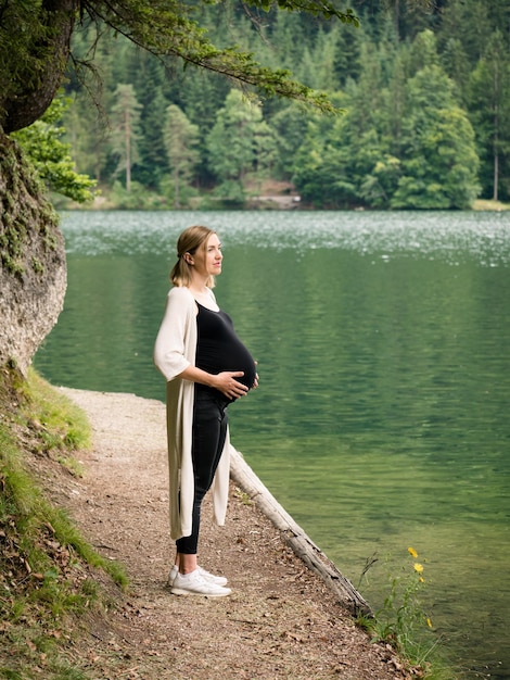 Linda e fofa mulher grávida perto de um lago de montanha na floresta.