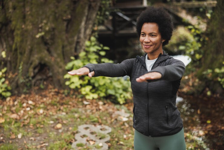Foto linda e madura mulher afro-americana sorridente se aquecendo e se alongando antes de correr de manhã nas montanhas.