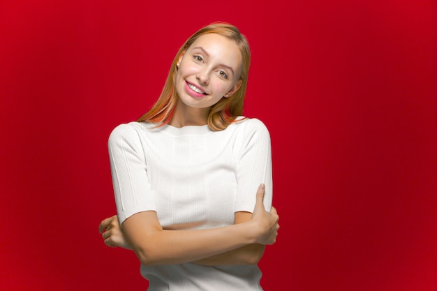 Linda e simpática jovem sorridente, olha para a câmera no fundo do estúdio vermelho, cuidados com a pele, mulheres