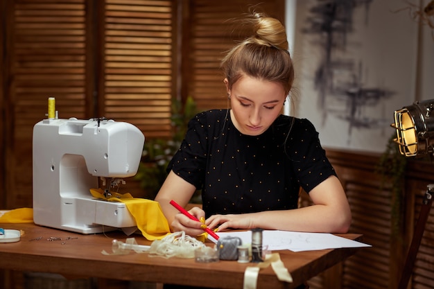 Linda e sorridente jovem costureira cria desenhos de roupas