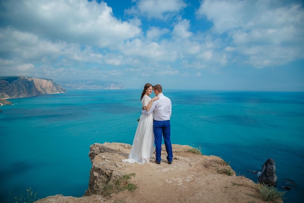 Linda e sorridente jovem noiva e noivo andando na praia beijando e se divertindo cerimônia de casamento perto das rochas e mar Cerimônia de casamento na costa de Chipre