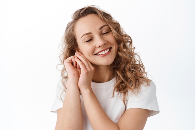 Linda e tenra mulher fecha os olhos e sonha acordado sorrindo de coração lembre-se de um feliz momento romântico em pé sobre fundo branco