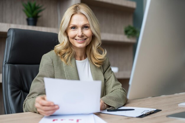 Linda empresária adulta madura com vestido elegante sentado na mesa do computador no escritório