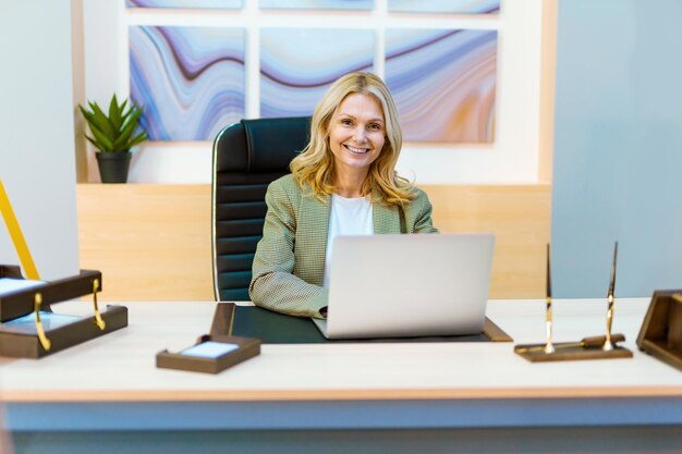 Linda empresária adulta madura com vestido elegante sentado na mesa do computador no escritório