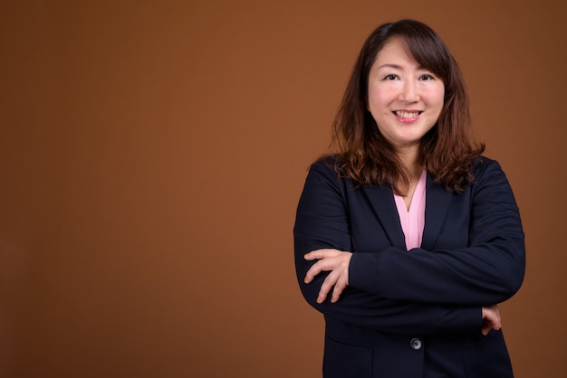 Linda empresária asiática de meia-idade contra uma parede marrom