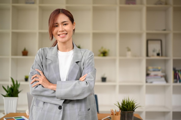 Linda empresária asiática em pé no local de trabalho do escritório com braços cruzados