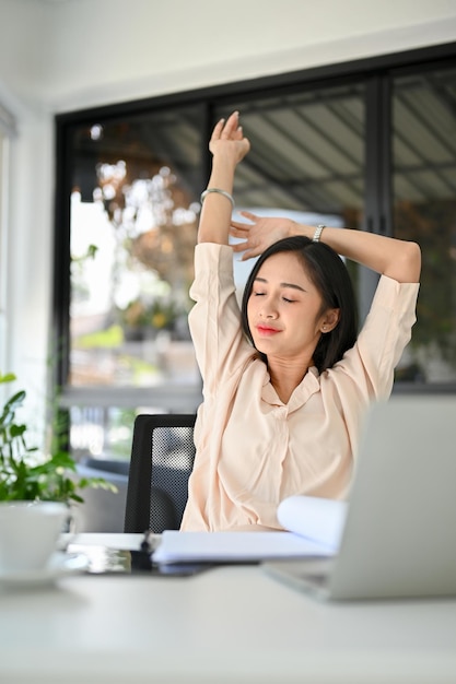 Linda empresária asiática milenar esticando as mãos relaxando em sua mesa de escritório