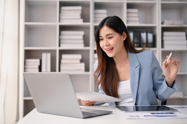 Linda empresária asiática olhando para a tela do laptop trabalhando em seu escritório