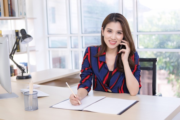 Linda empresária asiática segurando um smartphone para falar sobre trabalho, trabalho em casa