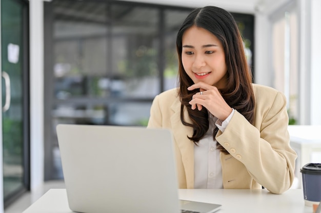 Linda empresária asiática trabalhando em suas tarefas de negócios no laptop em sua mesa