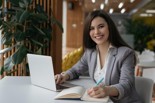 Foto linda empresária confiante usando laptop tomando notas trabalhando on-line no escritório