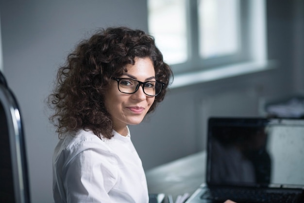 linda empresária morena encaracolada usando óculos no local de trabalho no escritório