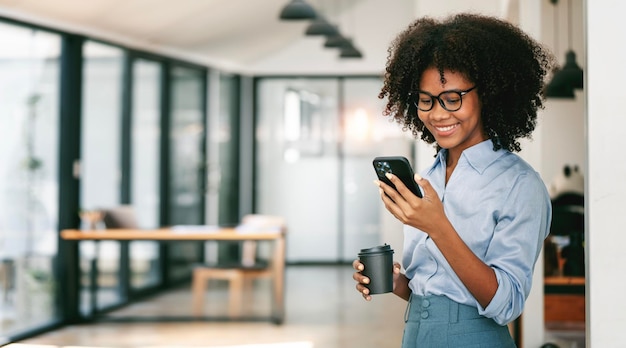 Linda empresária sorridente de cabelos cacheados usando smarphone no espaço de cópia do escritório