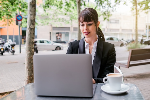 linda empresária usando laptop sentada em um café ao ar livre