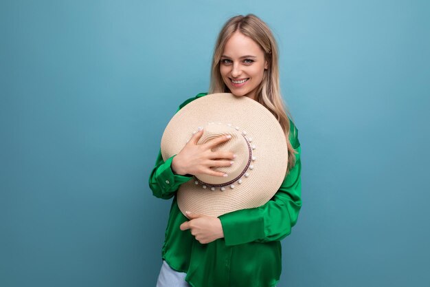 Linda y encantadora mujer adulta joven sosteniendo un sombrero de playa con un teléfono en sus manos sobre un fondo azul