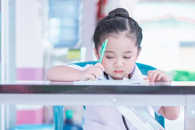 Una linda y encantadora niña asiática en uniforme de enfermera vestido escribiendo un informe