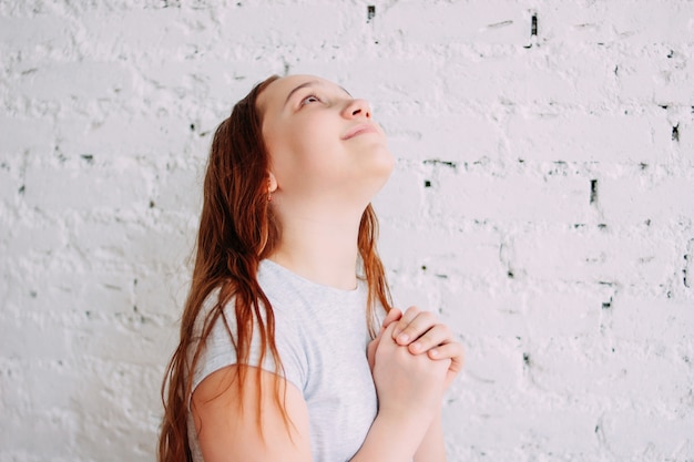 Foto linda encantadora ruiva sorridente garota adolescente fazendo um desejo isolado na parede de tijolo branco