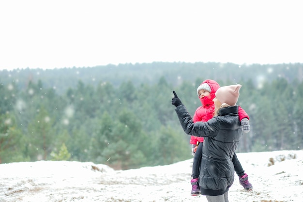 Linda escena idílica de una mujer llevando a una niña con ropa abrigada y mostrando copos de nieve y f de invierno