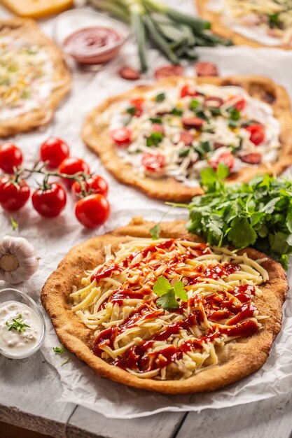 Linda escrivaninha de madeira cheia de langos e hangaria crocantes servidos com queijo, vegetais, presunto, ketchup, molhos, creme, alho e mantimentos sazonais.