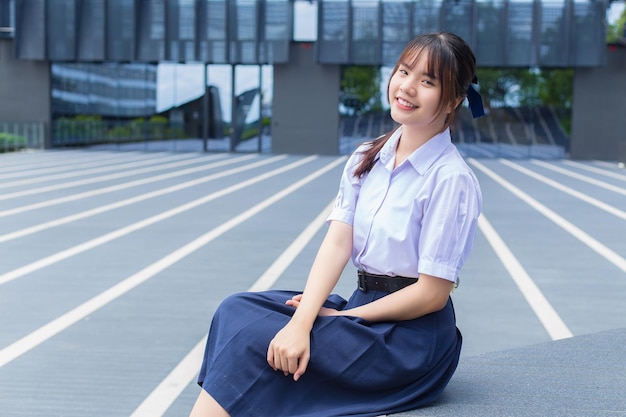 Linda estudante asiática do ensino médio em uniforme escolar com sorrisos confiantes enquanto ela alegremente