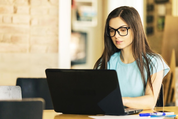 Foto linda estudante de cabelos escuros trabalhando no laptop em um escritório de coworking moderno e elegante