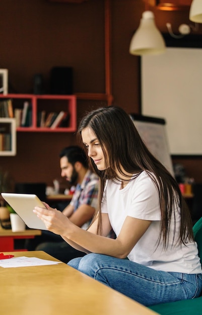 Linda estudante trabalhando com computador tablet sentado no escritório do café coworking