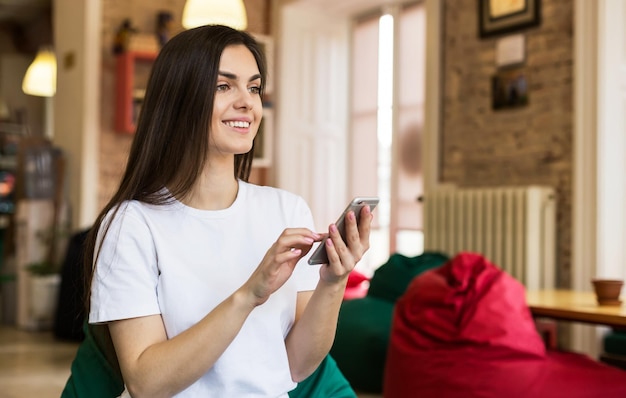 Linda estudante usando smartphone para mensagens de texto no escritório de coworking moderno e elegante