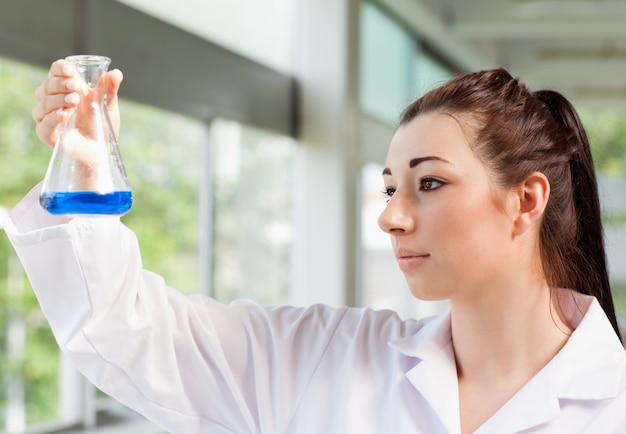 Linda estudiante de ciencias mirando un líquido azul