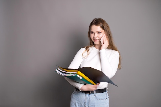 Una linda estudiante está hablando por teléfono y sosteniendo una carpeta abierta para documentos