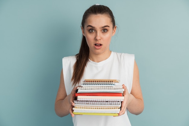 Linda estudiante con una montaña de cuadernos y libros en sus manos