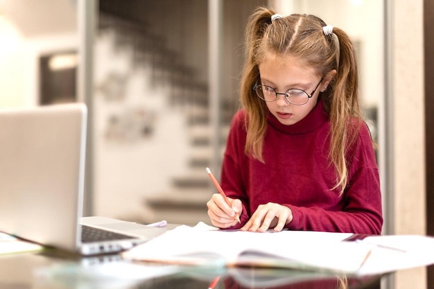 Foto linda estudiante niña seriamente haciendo la tarea usando una computadora portátil en casa aprendizaje a distancia para niños concepto de educación en línea