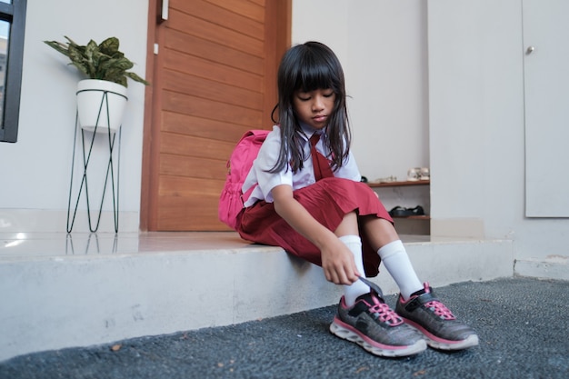 Linda estudiante de primaria se puso los zapatos. preparándose para ir a la escuela por la mañana