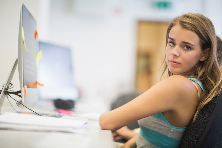 Foto linda estudiante que trabaja en la sala de ordenadores mirando a la cámara