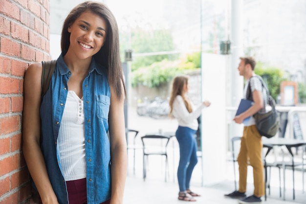 Linda estudiante sonriendo a la cámara con compañeros de clase detrás