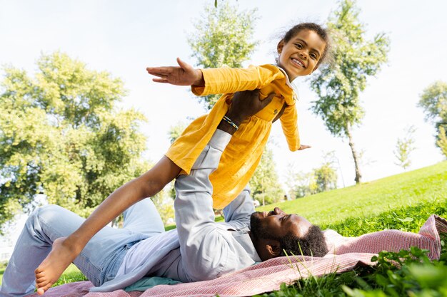 Foto linda família afro-americana feliz se unindo no parque - família negra se divertindo ao ar livre, pai brincando com sua linda filha
