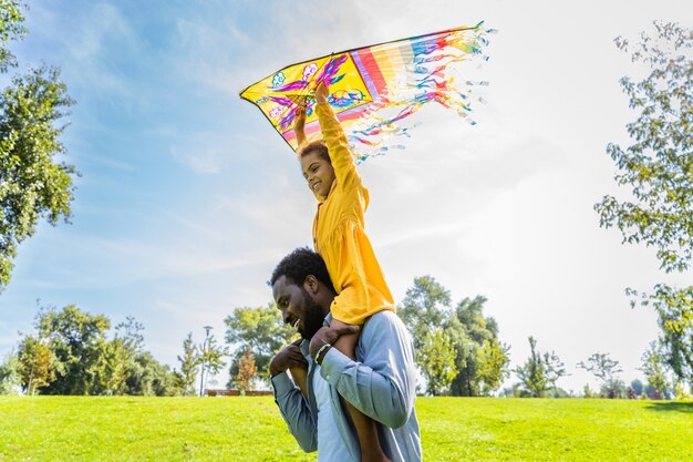 Foto linda família afro-americana feliz se unindo no parque - família negra se divertindo ao ar livre, pai brincando com sua linda filha