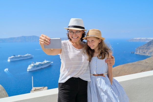 Linda família feliz, mãe e filha viajando juntos no mediterrâneo. tirando selfie usando smartphone, bela paisagem cênica com fundo de navios de cruzeiro, espaço de cópia