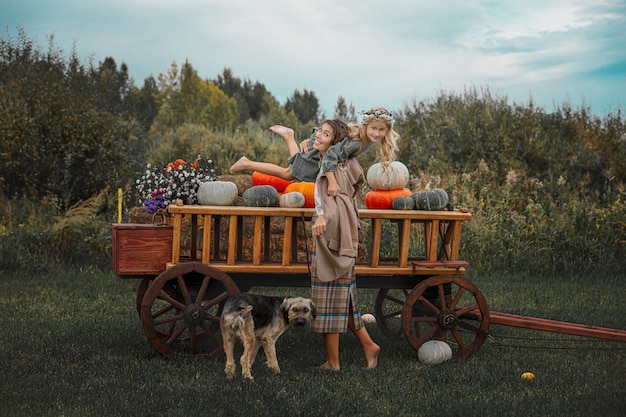 Linda família feliz, mãe, filha e cachorro de estimação juntos em um carrinho de madeira com abóboras