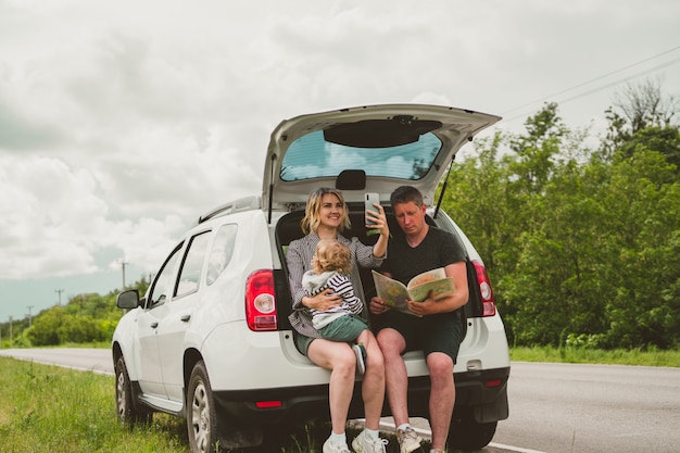 La linda familia feliz de papá, mamá e hijo está viajando en automóvil y se detuvo al costado de la carretera para ver el mapa.