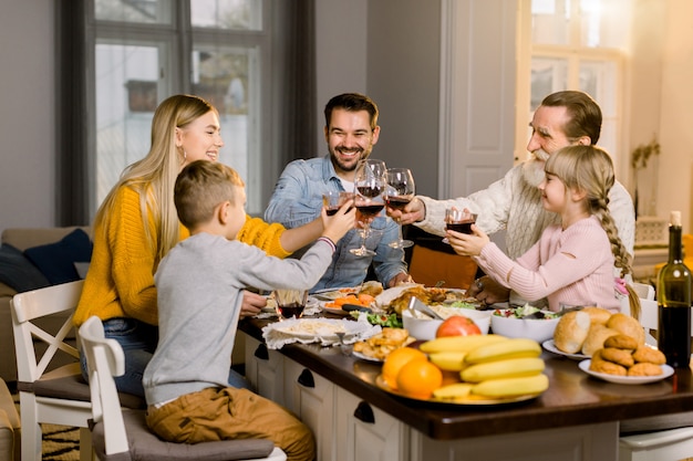 Linda família feliz tilintar de copos de vinho e suco no jantar de férias