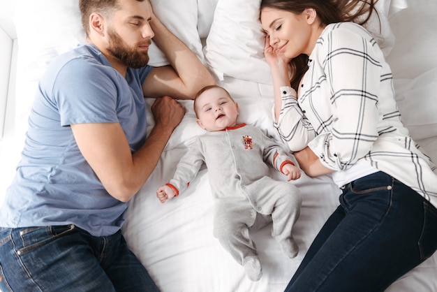 Linda familia joven. Los padres se acuesta en la cama con su pequeño hijo.